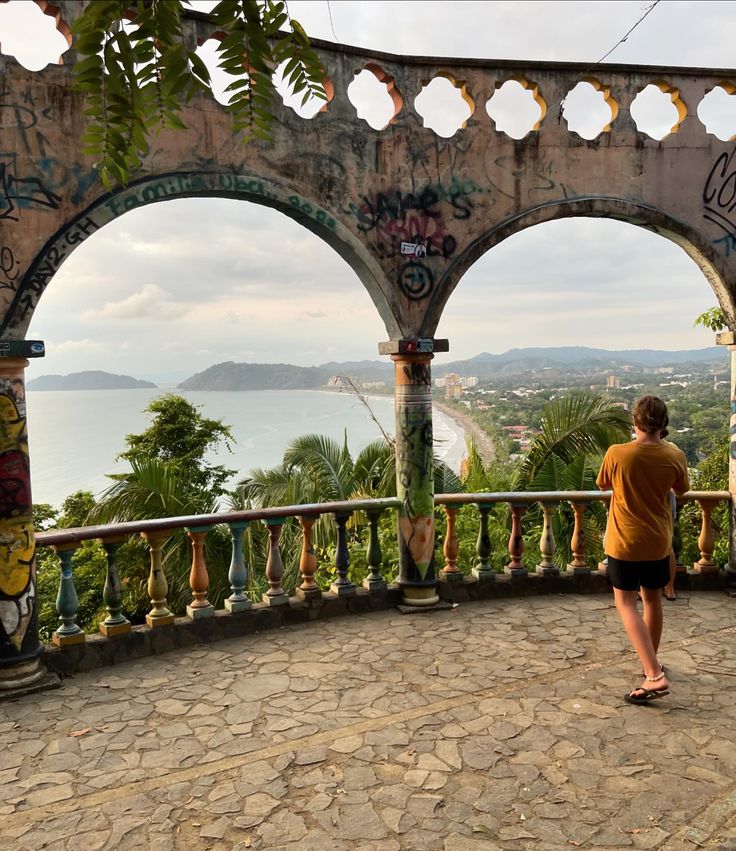 a man standing on top of a stone walkway next to a lush green forest covered hillside