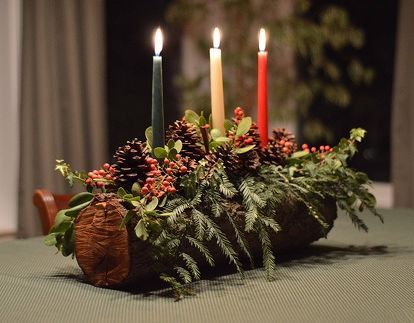 candles are lit on a log with greenery and pine cones