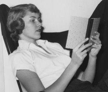 a woman sitting in a chair reading a book with her eyes closed while holding a box