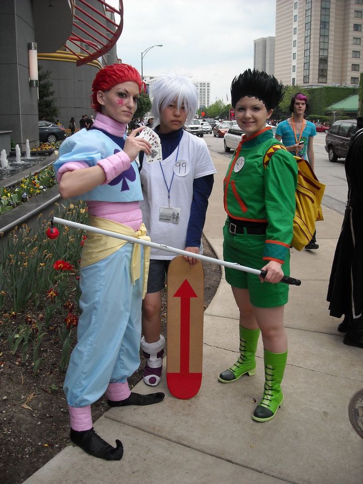 three people dressed up in costumes standing on the sidewalk with one person holding a sign