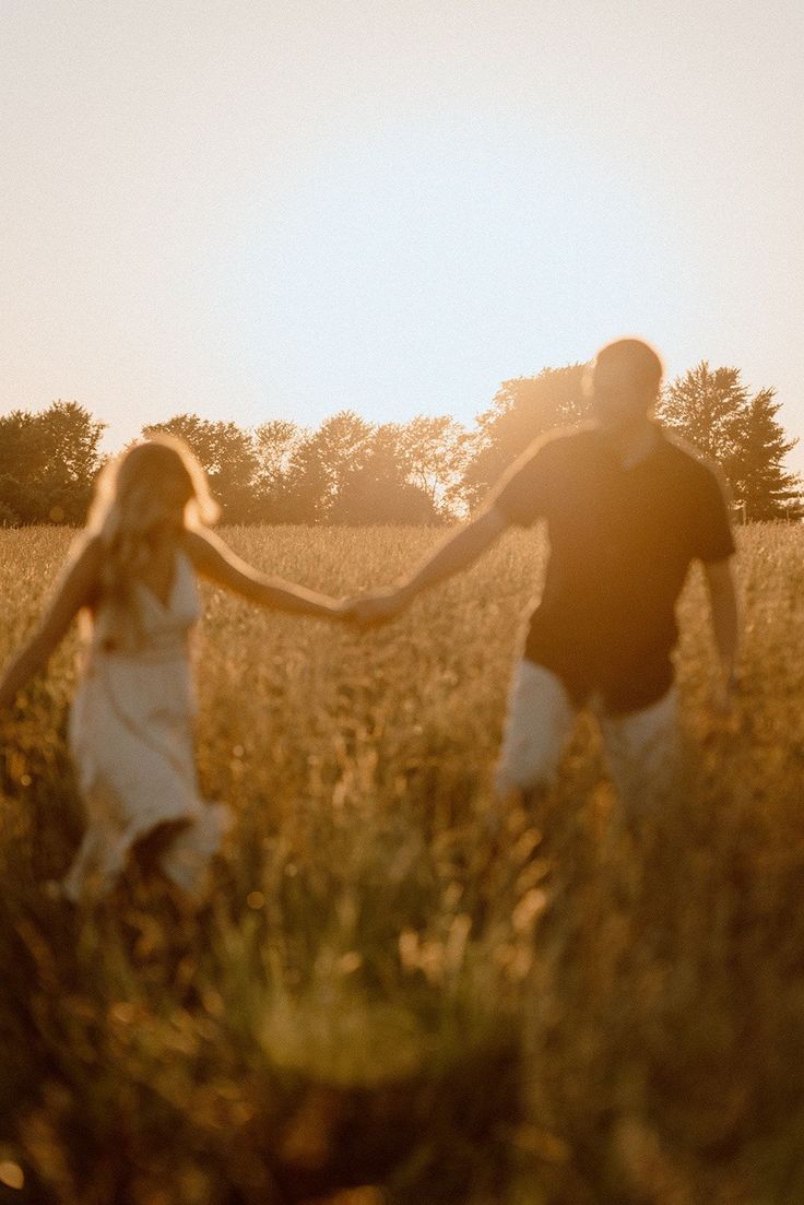 a man and a woman holding hands in a grassy field with the sun behind them