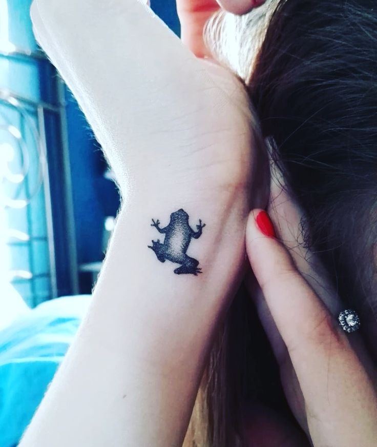 a woman's arm with a small frog tattoo on the left side of her wrist