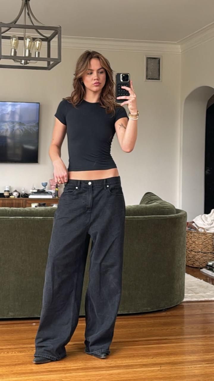 a woman taking a selfie in her living room while wearing high waisted jeans