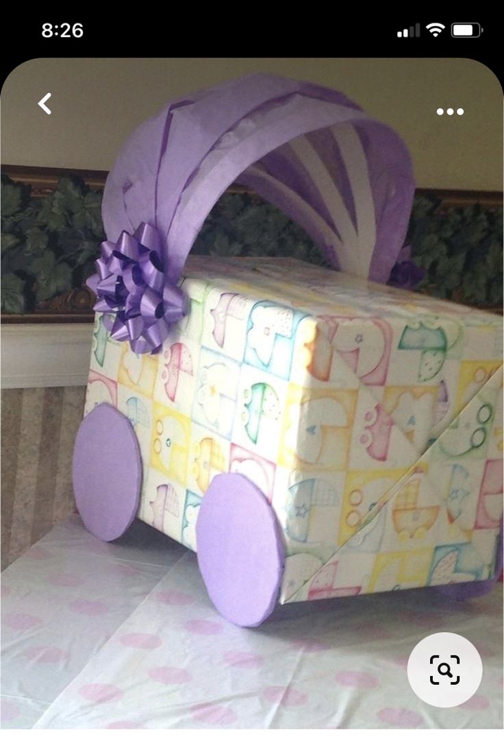 a present wrapped in paper with purple ribbon and bow on it sitting on a table