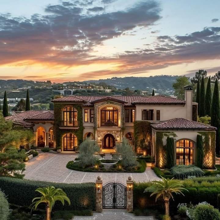 an aerial view of a large home with trees and bushes in front of it at sunset