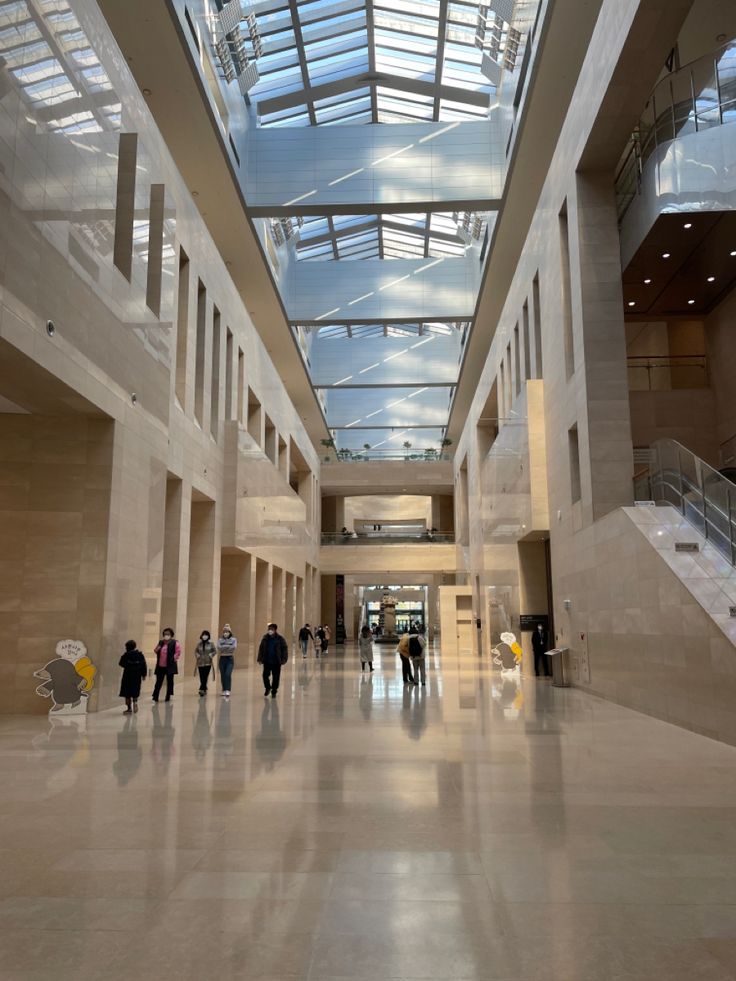 several people are walking around in a large building with skylights above them and stairs leading up to the second floor