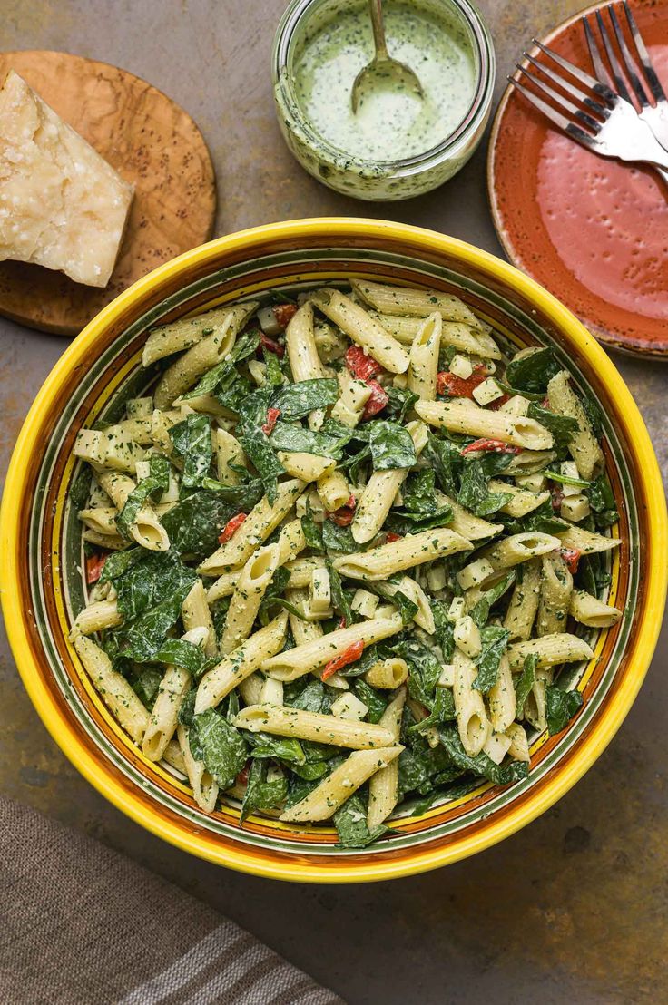 a yellow bowl filled with pasta and spinach next to two plates of pita bread