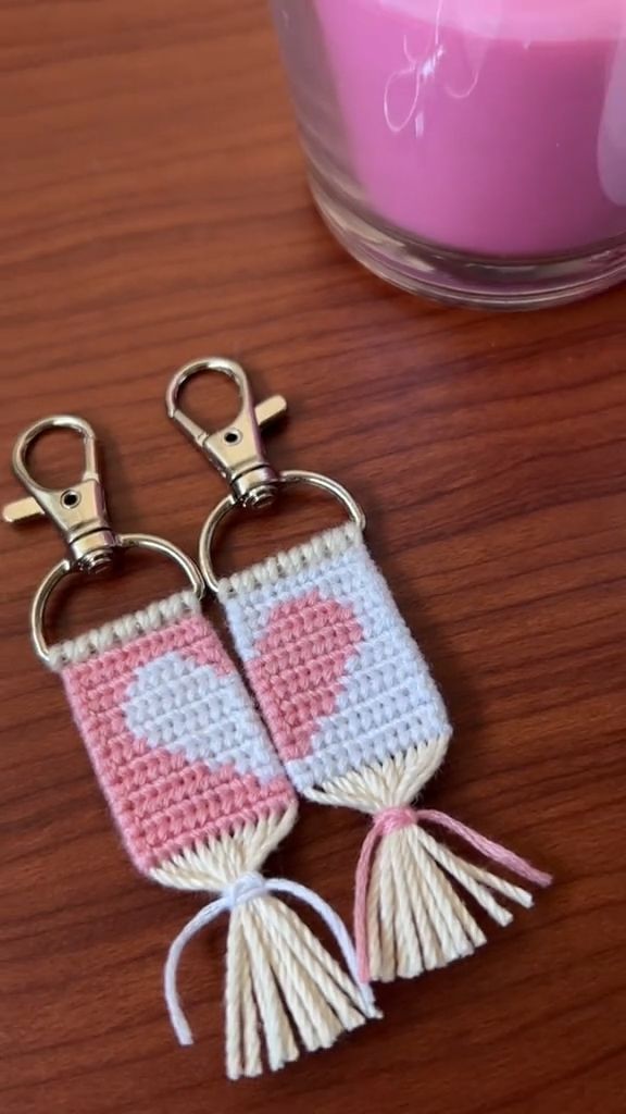 two crocheted key chains sitting on top of a table next to a candle