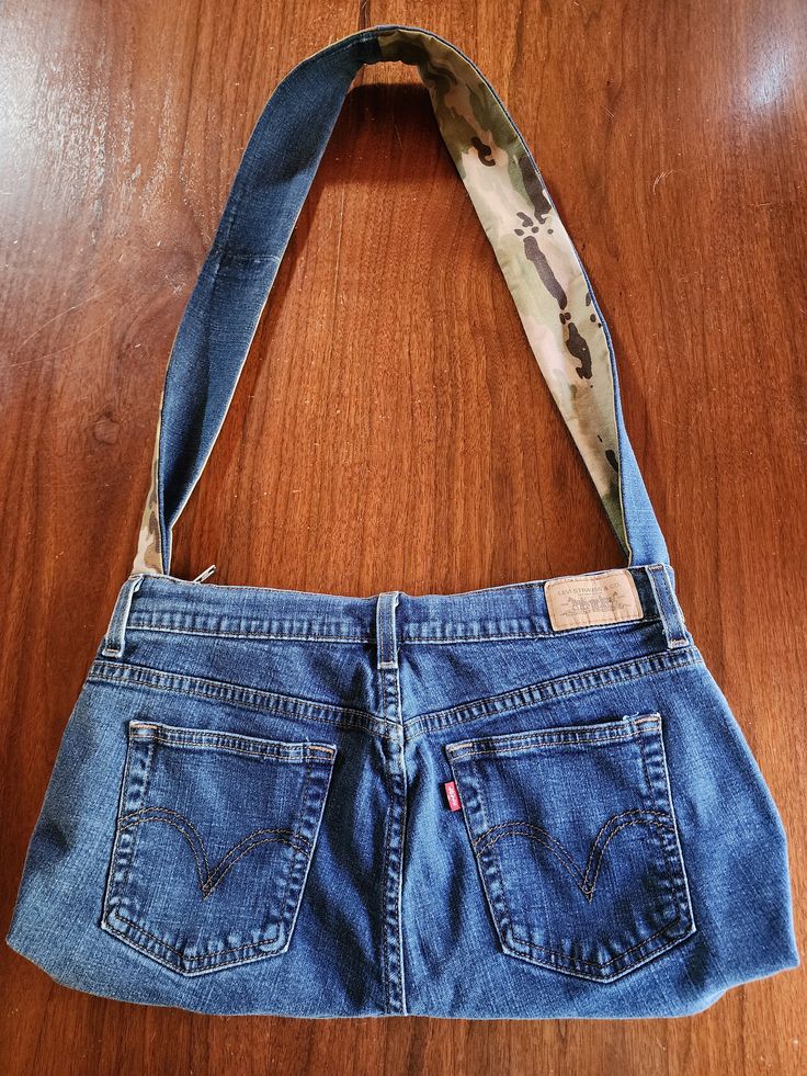 an old pair of blue jeans is being held up by a handbag on a wooden surface