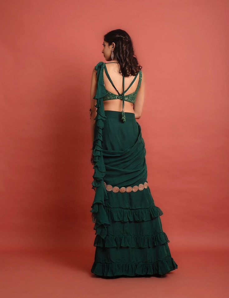 Dark green sequin and thread embroidered georgette blouse with attached soft organza ruffle at shoulder at the back, pre-pleated at center soft organza skirt with frill details and soft organza pre-pleated detachable pallu at waist and shoulder with gold lace embellishment.Dry Clean only. Festive Green Pre-draped Saree With Ruffles, Green Ruffled Sets With Traditional Drape, Party Dress With Unstitched Chiffon Blouse, Green Georgette Set With Ruffles, Green Organza Blouse Piece For Party, Georgette Ruffle Dress For Reception, Wedding Georgette Blouse With Ruffles, Evening Organza Lehenga With Ruffles, Wedding Georgette Ruffled Blouse