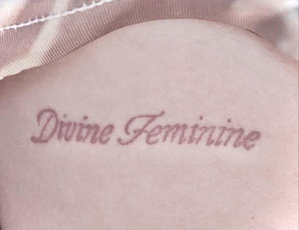 a woman with a tattoo that reads divine feminine