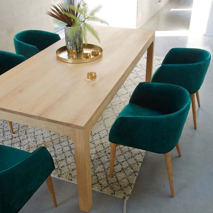 a wooden table surrounded by green chairs in a room with a rug on the floor