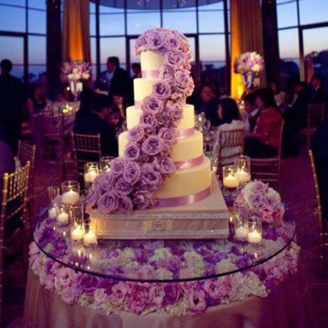 a wedding cake with purple flowers and candles on the table in front of an audience