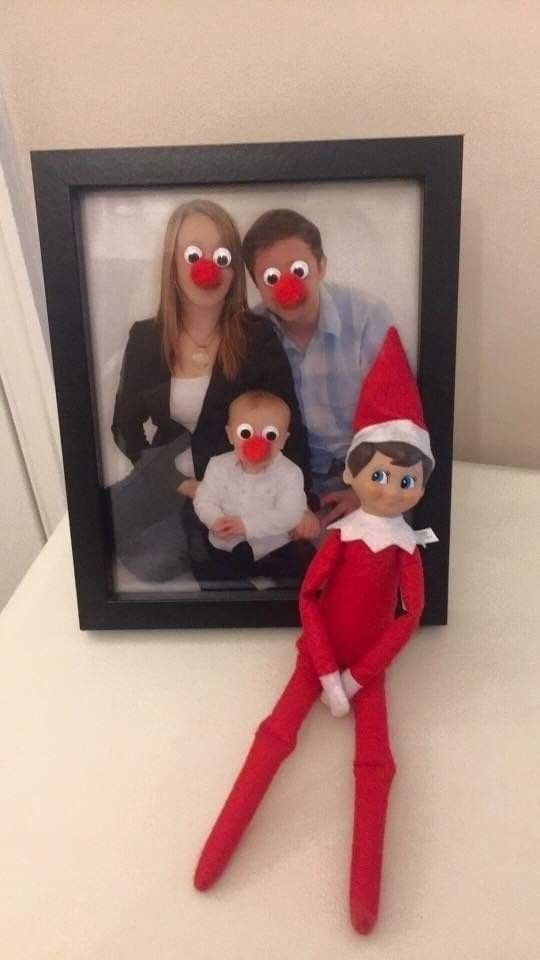 an elf with two red noses is posed in front of a photo frame, holding a baby