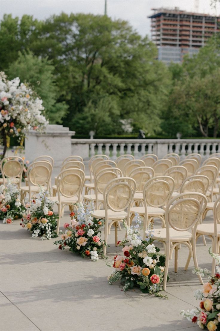 rows of chairs lined up with flower arrangements on the back and sides for an outdoor ceremony