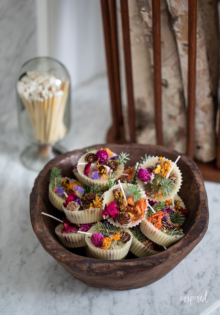 a wooden bowl filled with cupcakes covered in edible flowers and pine cones on top of a marble counter