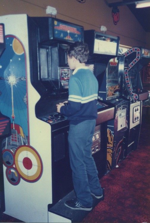 a young man standing in front of an arcade machine