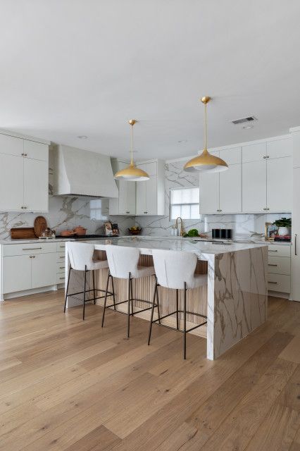 a large kitchen with marble counter tops and white cabinets, along with bar stools