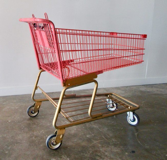 a red shopping cart sitting on top of a cement floor next to a white wall