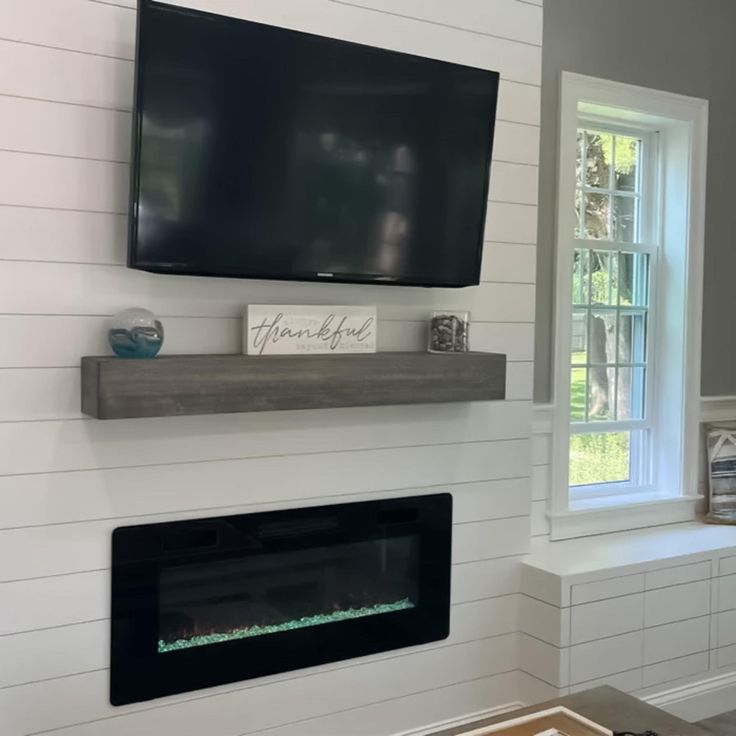 a flat screen tv mounted on the wall above a fireplace in a room with white walls