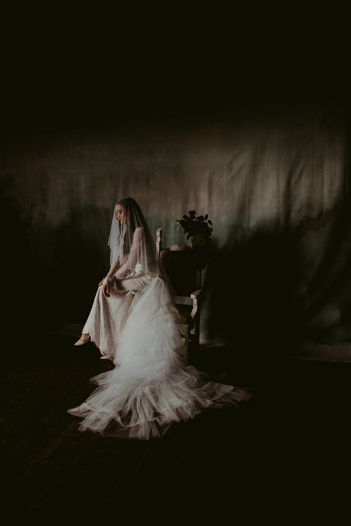 a woman in a wedding dress is sitting on a chair with her veil pulled back