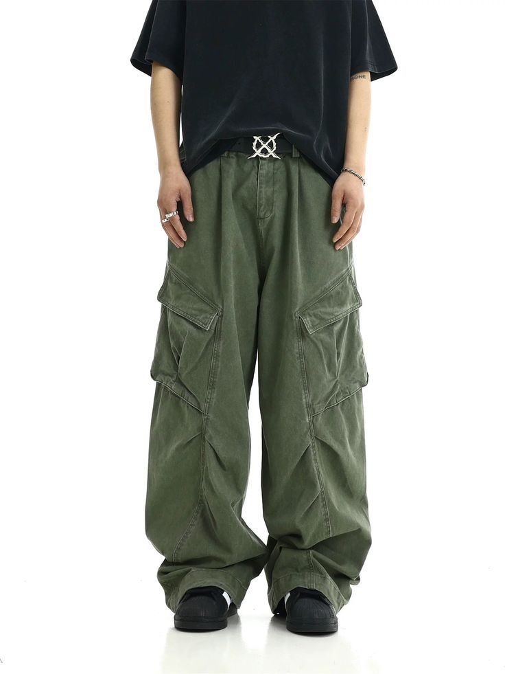 a man standing in front of a white background wearing green cargo pants and a black t - shirt