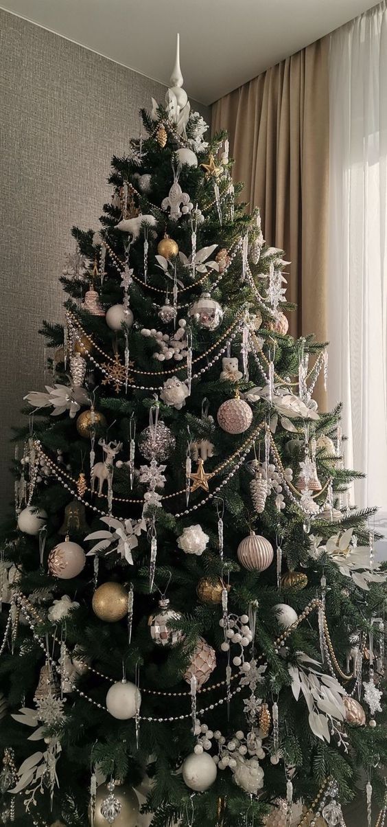 a decorated christmas tree in a living room with gold and white ornaments on the top