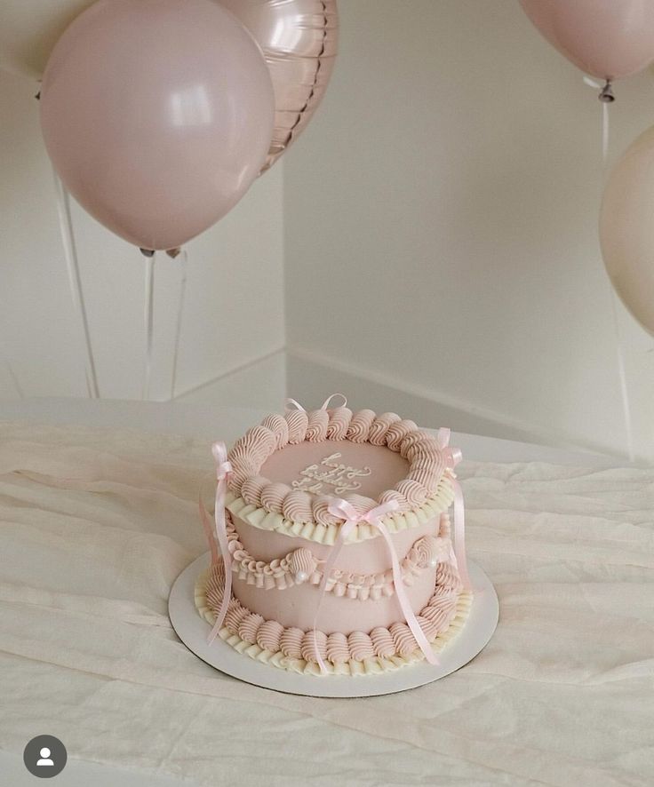 a pink cake sitting on top of a white table next to balloons and streamers