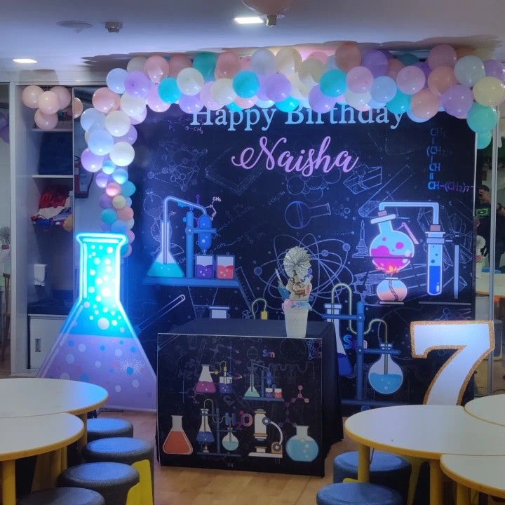 a birthday party with balloons and science themed decorations on the wall, including a blackboard