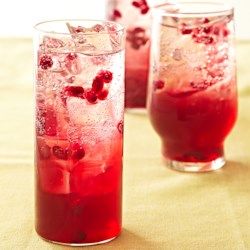 two glasses filled with red liquid and ice on top of a yellow cloth covered table