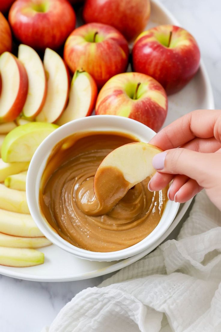 an apple being dipped into caramel sauce in front of apples on a white plate