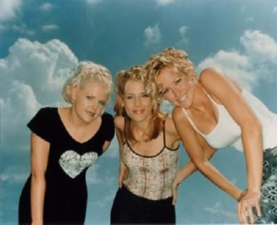 three women posing for a photo in front of the sky and clouds with their arms around each other