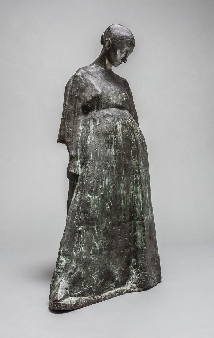 a bronze statue of a woman with her hands in her pockets, standing against a gray background