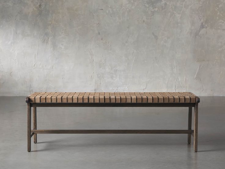 a bench made out of woven material and wood frame, against a concrete wall with no one sitting on it