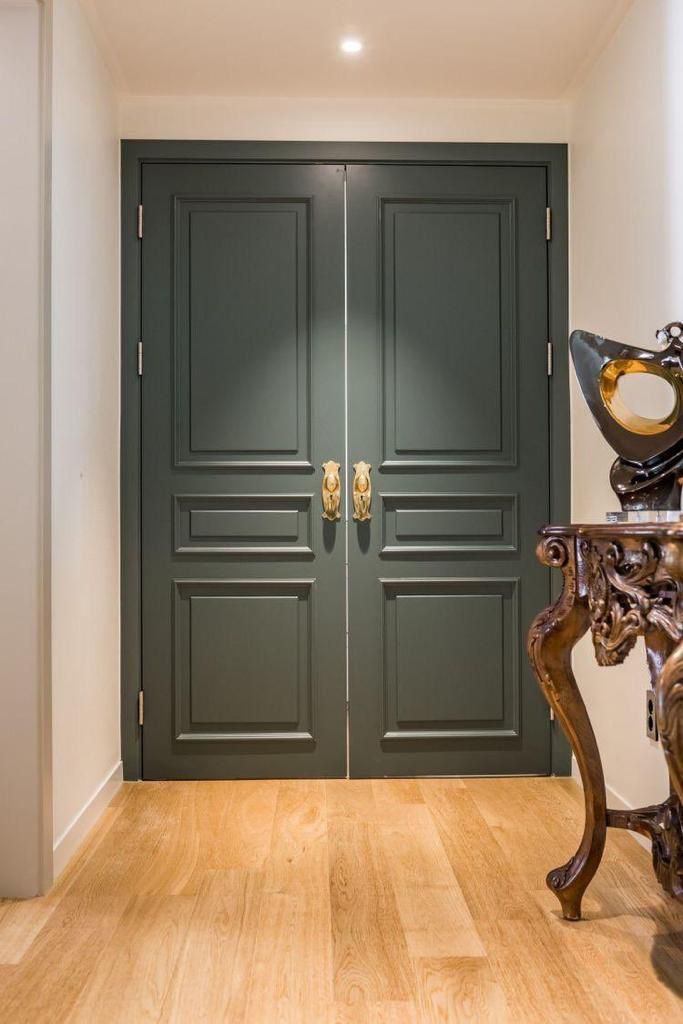 two green doors in an entry way with wooden flooring and gold accents on either side