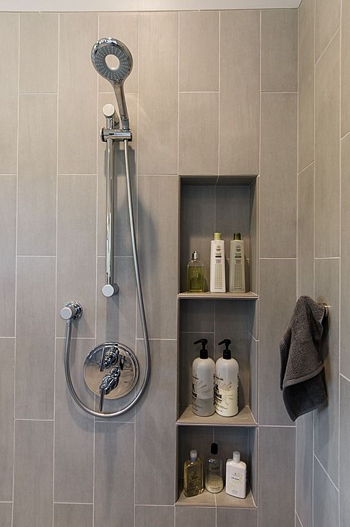 a bathroom with gray tile and white fixtures, including a shower head, soap dispenser, hand sanitizer, and towel rack