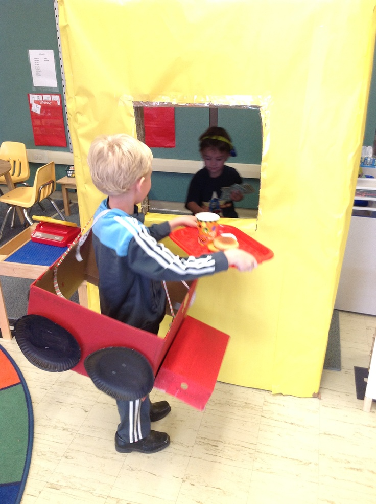 two children are playing with toys in a play area at the elementary school, one boy is holding a tray and another child is sitting on a chair