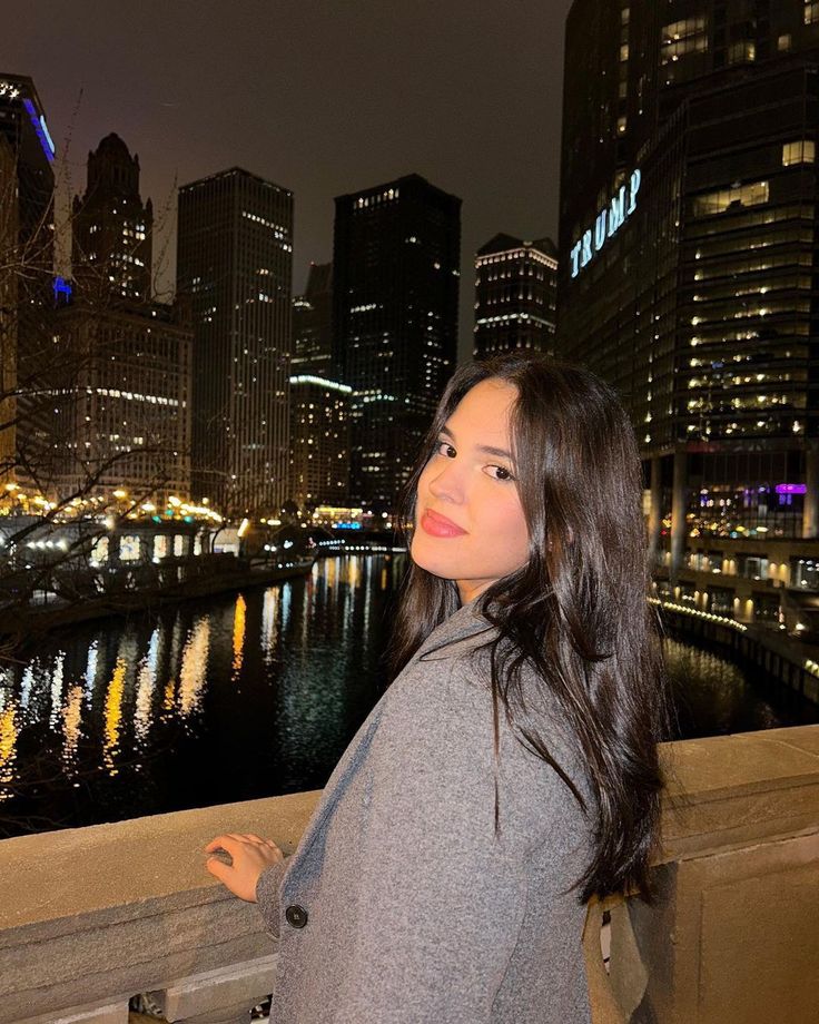 a beautiful young woman standing on top of a bridge next to a river at night