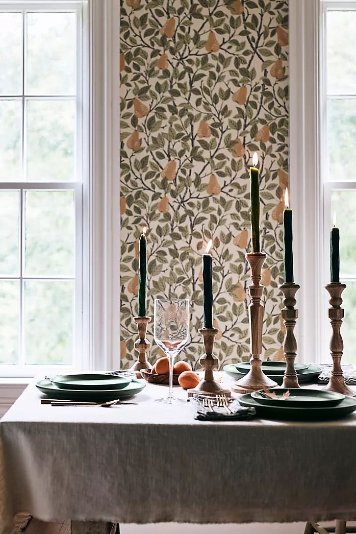 the table is set with plates, candles and fruit in front of a wallpapered window