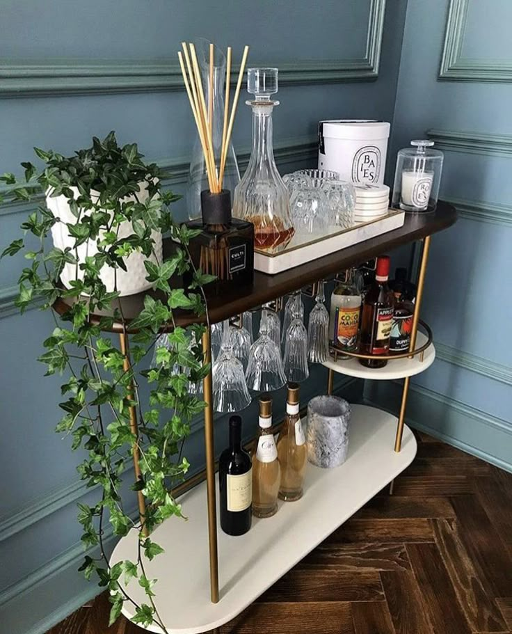 a bar cart filled with liquor bottles and glasses on top of a wooden floor next to a potted plant