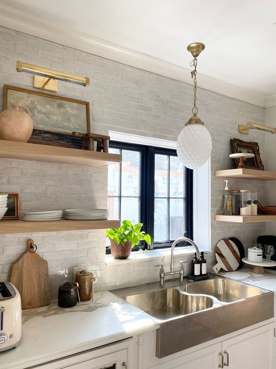 a kitchen with white cabinets and open shelving on the wall, along with a stainless steel sink