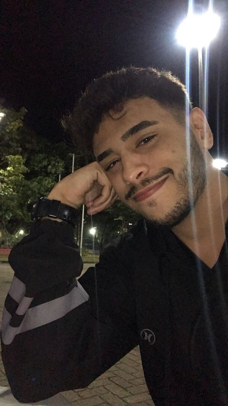 a young man is posing for the camera at night with his hand on his head