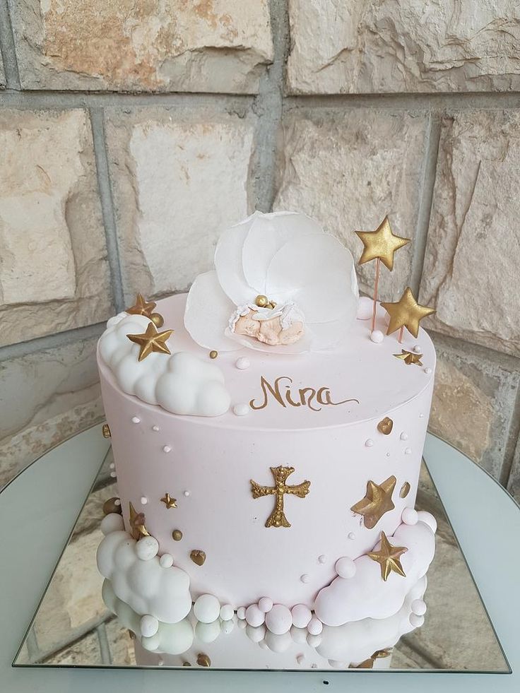 a pink and white cake with gold stars on it sitting on a table next to a brick wall