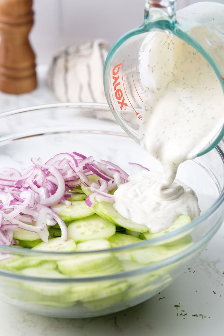 a bowl filled with cucumbers and onions being drizzled with dressing