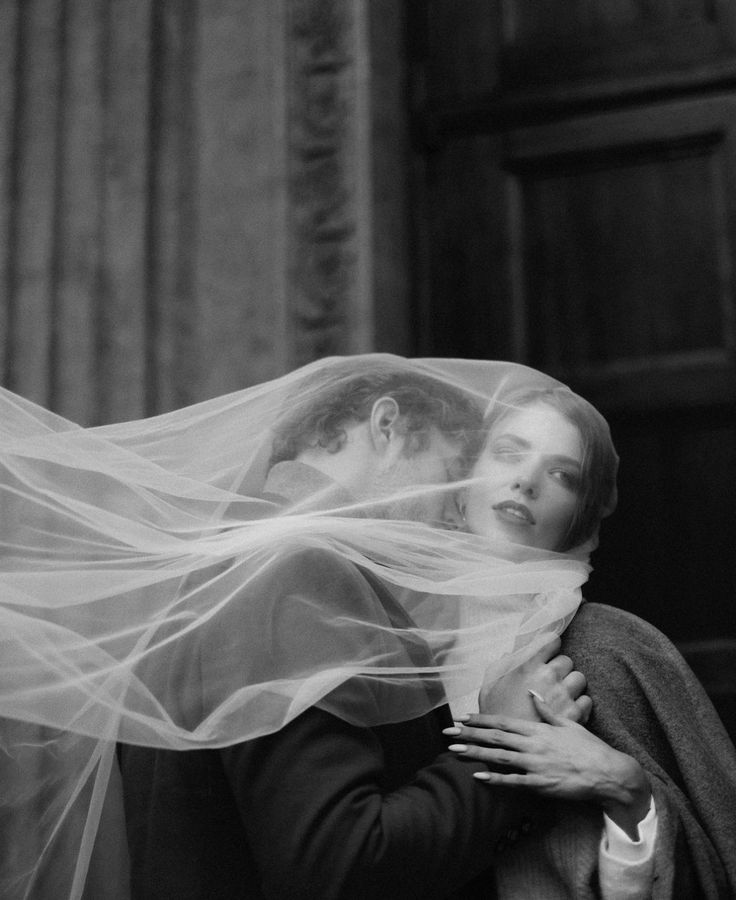 black and white photograph of a bride and groom with veil blowing in the wind over their heads