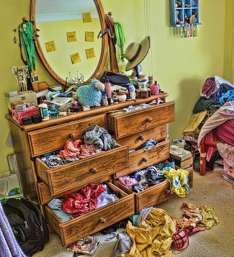 the dresser is full of clothes and clutter in front of a large round mirror