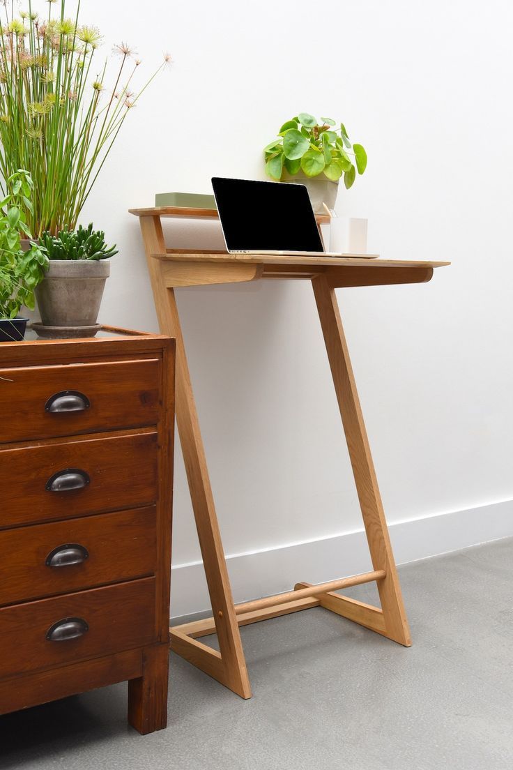 a wooden desk with a laptop on it next to a potted plant and dresser