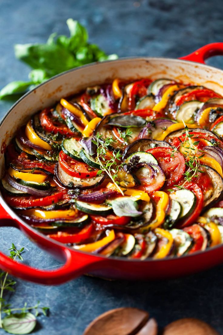 a red pan filled with sliced vegetables on top of a table next to wooden spoons