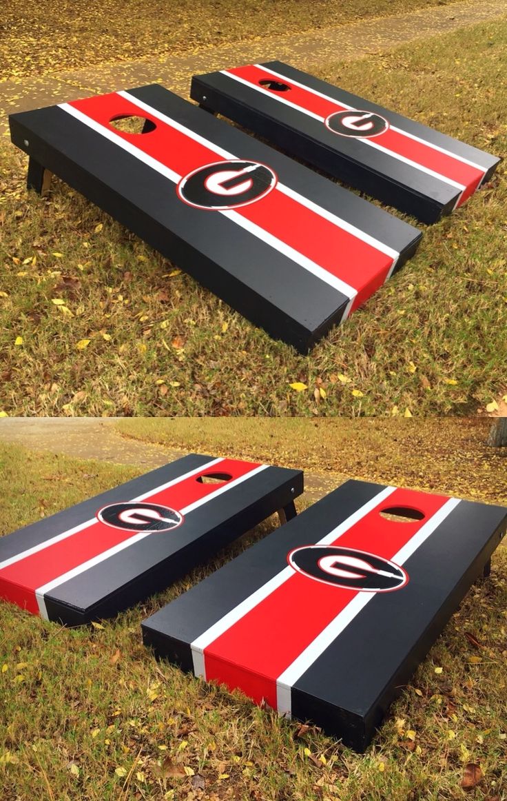 two cornhole game boards sitting on top of the grass with red and black stripes