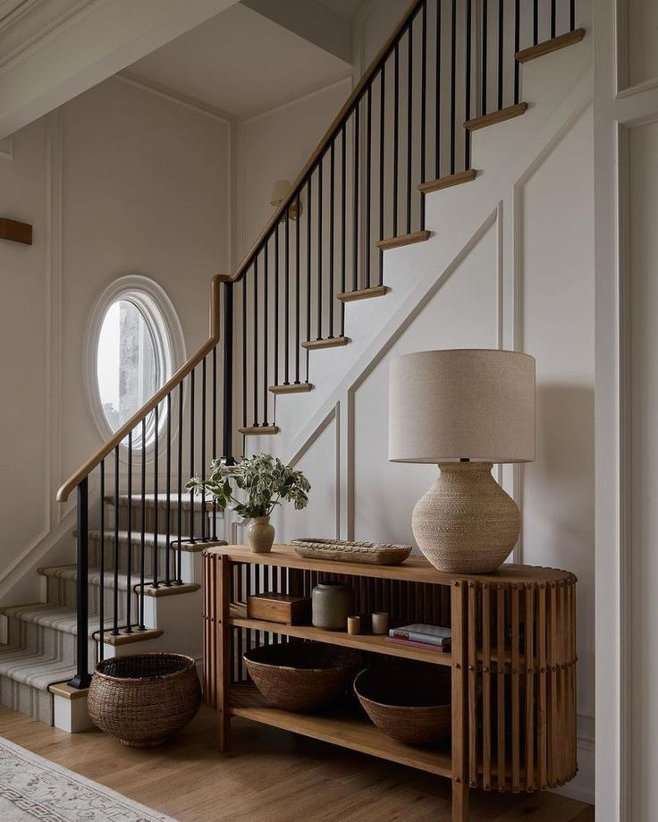 a wooden table sitting under a stair case next to a lamp on top of a hard wood floor